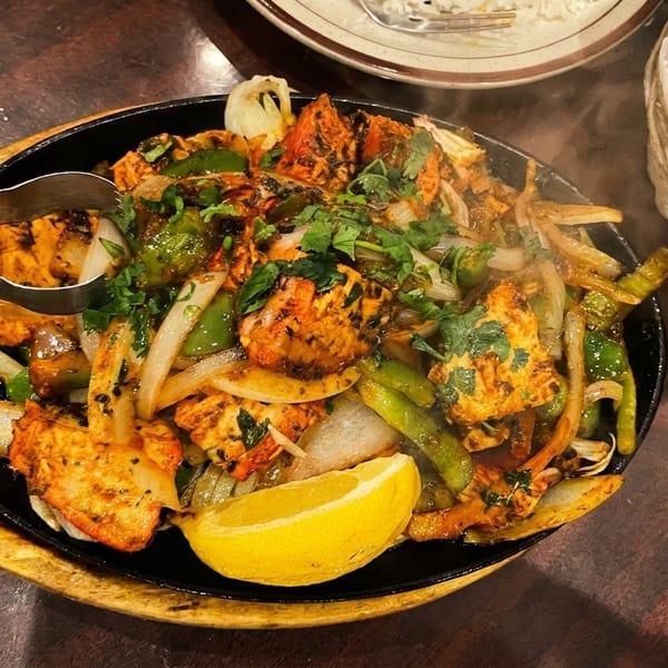 Sizzling chicken tikka with onions, peppers, cilantro, and a lemon wedge, served with naan.