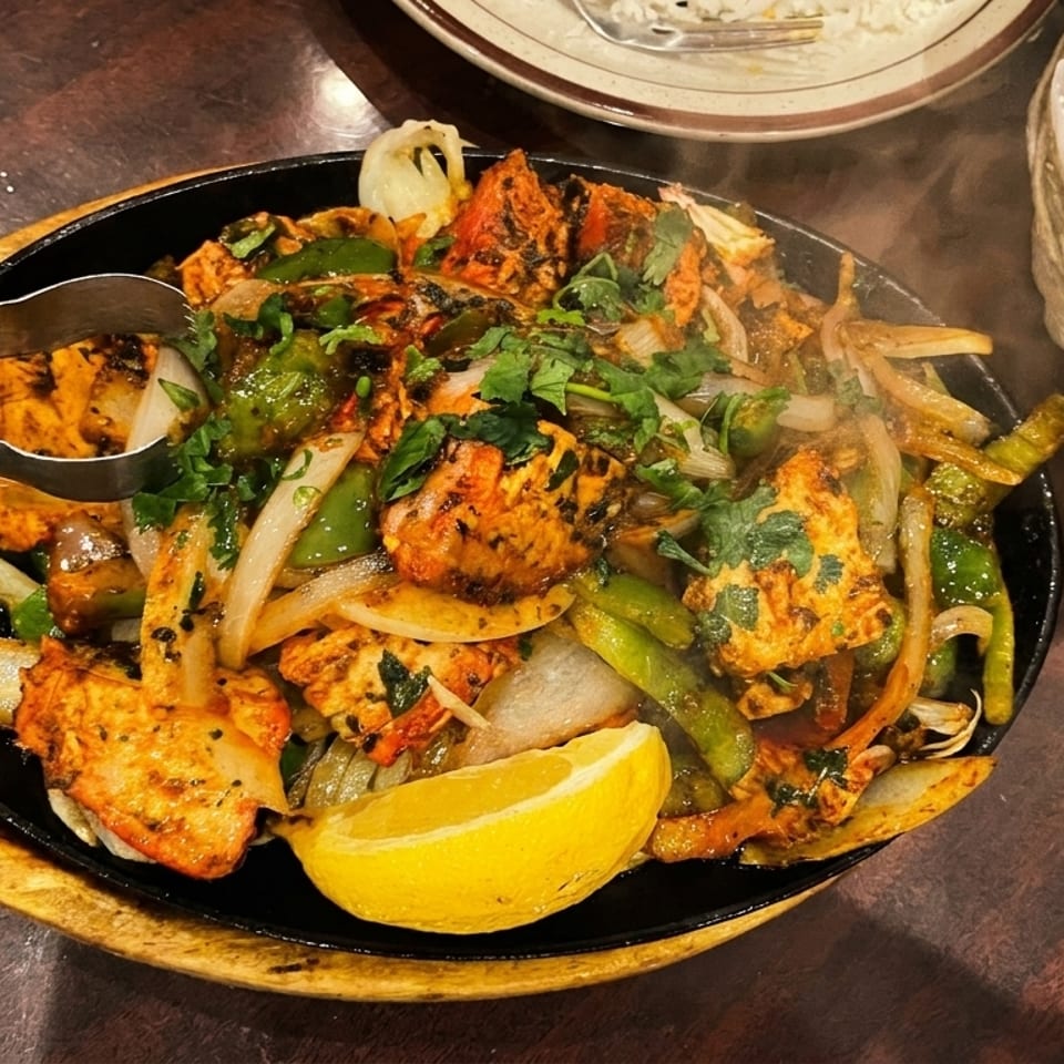Sizzling chicken tikka with onions, peppers, cilantro, and a lemon wedge, served with naan.