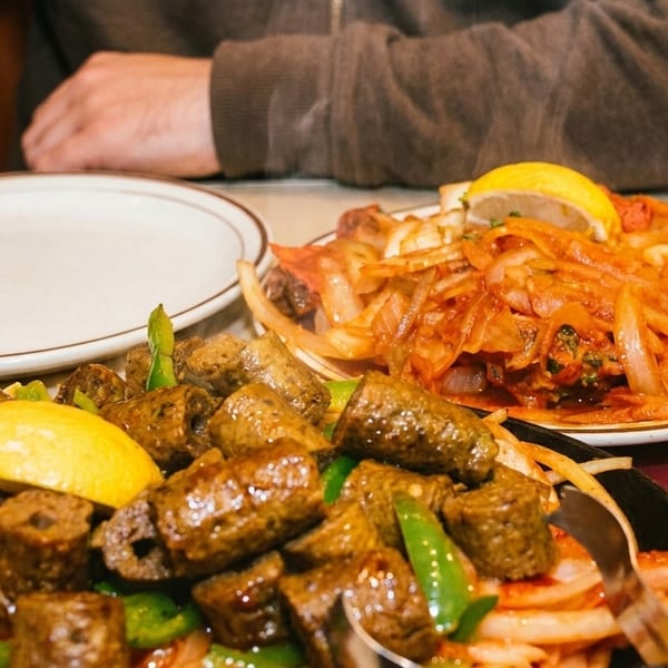 Two plates of Indian food, one with seekh kebabs and the other with chicken tikka, on a table.