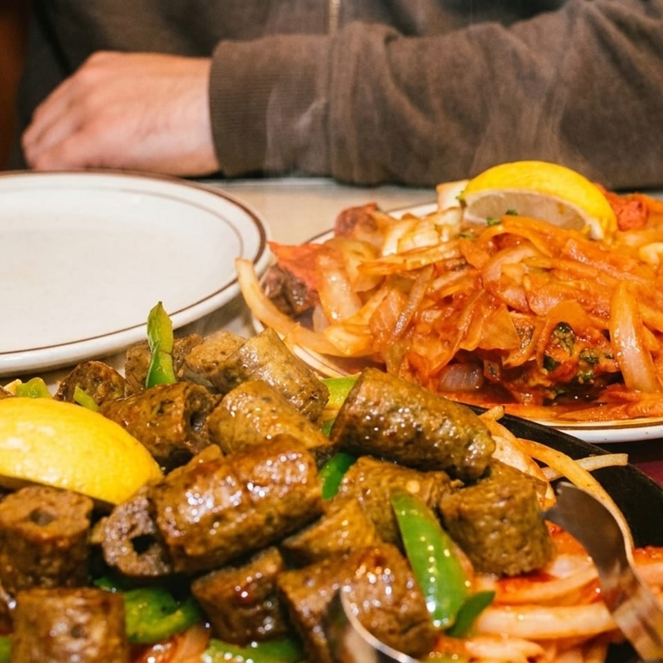 Two plates of Indian food, one with seekh kebabs and the other with chicken tikka, on a table.